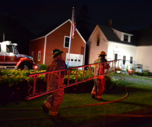 Bristol firefighters carry a ladder on the scene of a house fire at 2189 Bristol Road in Pemaquid the evening of Friday, July 19. (Maia Zewert photo)