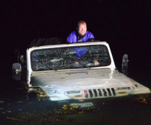 Local diver David Gallagher steers a Jeep Wrangler as a truck pulls it out of the water at Eugley Landing in South Bristol the night of Monday, July 29. Quick Turn Auto Repair and Towing Inc., of Damariscotta, pulled the Jeep out. (Evan Houk photo)