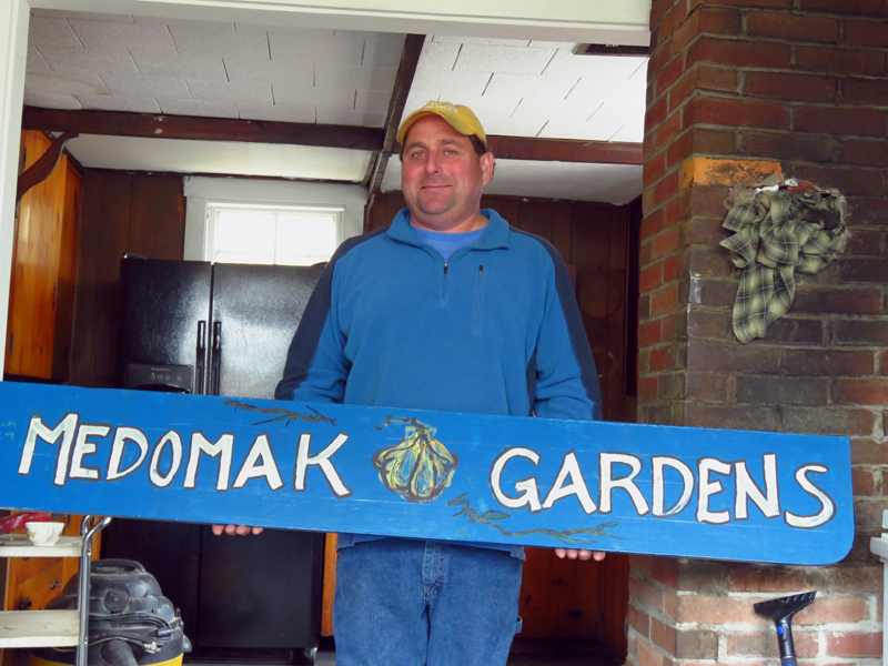 Tony Gallace holds a "Medomak Gardens" sign. Gallace manages the Feed the Need program, which is partnering with other local organizations to launch the Edible Waldoboro program.