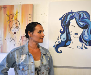 Whitefield artist Manda Hard poses between her paintings "Teacher Girl" (left) and "Water Girl" at the opening reception for her art exhibit at Sheepscot General in Whitefield on Friday, Aug. 2. (Christine LaPado-Breglia photo)
