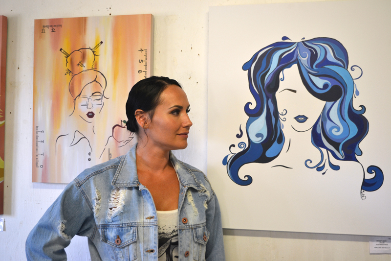 Whitefield artist Manda Hard poses between her paintings "Teacher Girl" (left) and "Water Girl" at the opening reception for her art exhibit at Sheepscot General in Whitefield on Friday, Aug. 2. (Christine LaPado-Breglia photo)