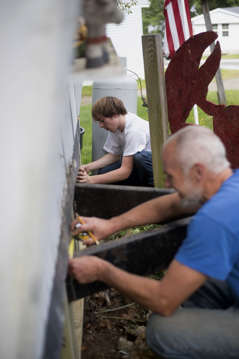 Shane Woods, back, a recent graduate of Medomak Valley High School, and Bill Hinkley, a teacher at the school, work to replace the skirt on Woods' home Sunday, Sept. 8. (Jessica Picard photo)