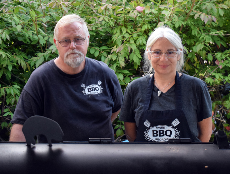 Ken Flower, owner of Sweet Georgia BBQ, stands with Susan Concolino behind his wood-fired smoker. The barbecue stand has moved from Bristol to a new location in the parking lot of Milling Around at 67 Main St. in Newcastle. (Evan Houk photo)