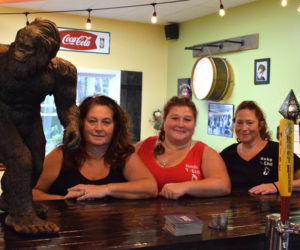 From left: Y-Knot Underground co-owners Carol Heaberlin, Mindy Jones, and Elayne Trotta sit at the bar next to the new Damariscotta eatery's mascot, Bigfoot. (Evan Houk photo)