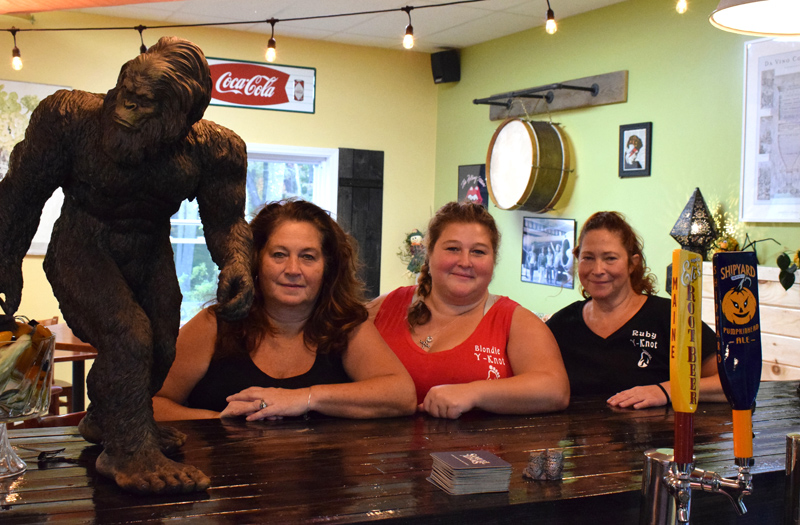 From left: Y-Knot Underground co-owners Carol Heaberlin, Mindy Jones, and Elayne Trotta sit at the bar next to the new Damariscotta eatery's mascot, Bigfoot. (Evan Houk photo)