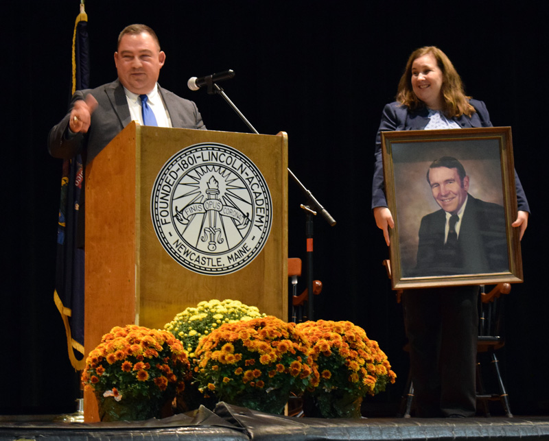 Lincoln Academy Board of Trustees President Judi Hilton holds up a portrait of the late LA Principal Arthur Dexter as LA graduate and Maine District Court Judge Eric J. Walker tells a story about Dexter during the installation ceremony for new Head of School Jeffrey Burroughs on Saturday, Oct. 5. (Evan Houk photo)