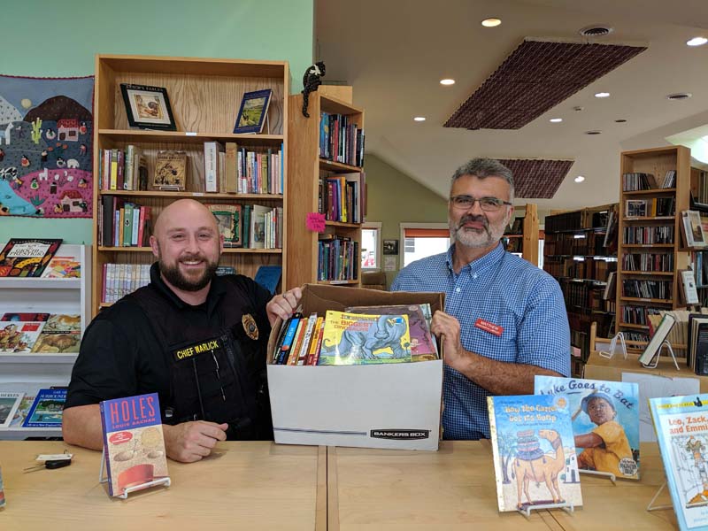 Skidompha Library Executive Director Matthew Graff (right) hands off books from the Skidompha Secondhand Book Shop to Damariscotta Police Chief Jason Warlick.