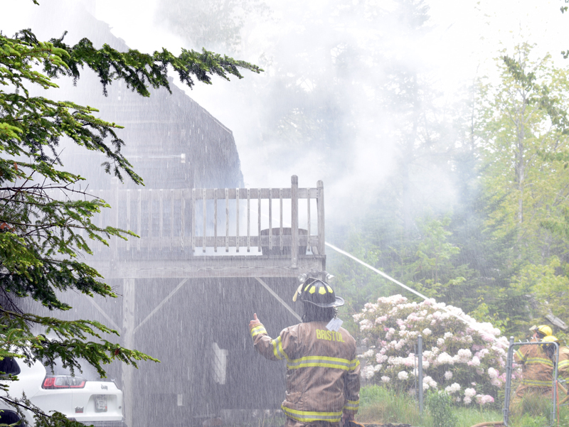 A Bristol firefighter directs the stream from a deck gun on top of a fire truck at a house fire at 159 McFarland Shore Road in New Harbor the moring of Wednesday, June 3. Bristol Fire Chief Paul Leeman Jr. said the house was a total loss. (Evan Houk photo)