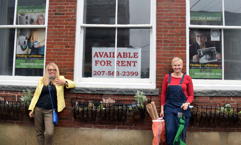 Finding Our Voices founder Patrisha McLean (left) stands with local volunteer coordinator Eve Jamison in front of 17 Elm St. in Damariscotta on Thursday, June 11. The duo hung nearly 50 banners in Damariscotta and Boothbay Harbor, including the one featuring McLean in the window at left. (Evan Houk photo)