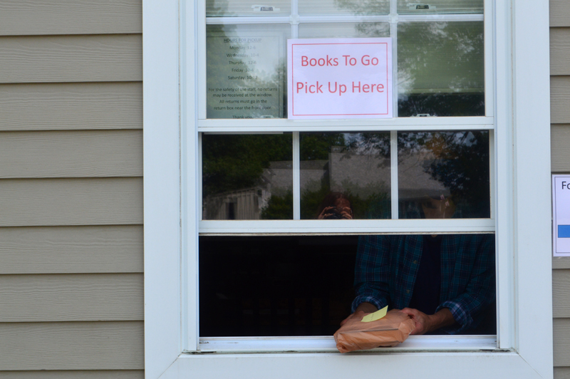 Cathrina Skov, director of the Waldoboro Public Library, passes a bag of books through her library's curbside pickup window. The library has been offering curbside service since May 12. (Alyce McFadden photo)