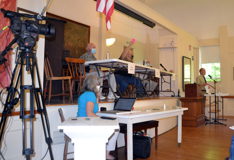 Westport Island Third Selectman Ross Norton raises his card in opposition to accepting a section of North End Road as a town way during annual town meeting at the historic town hall, Saturday, July 18. COVID-19 precautions at the meeting included face masks, Plexiglas barriers in front of the moderator and selectmen, and audiovisual equipment to connect voters at the town hall with those present in the community church next door. (Charlotte Boynton photo)