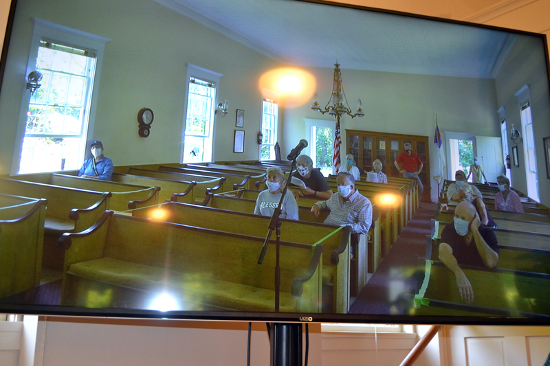 A screen at the historic town hall displays voters in the community church next door during Westport Island's annual town meeting Saturday, July 18. In a unique approach to physical distancing, audiovisual equipment connected voters in the church with those in the town hall. (Charlotte Boynton photo)