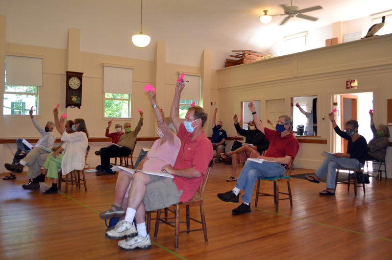 Westport Island voters sit well apart and wear face masks as they raise their hands to accept a section of North End Road as a town way during annual town meeting, Saturday, July 18. (Charlotte Boynton photo)