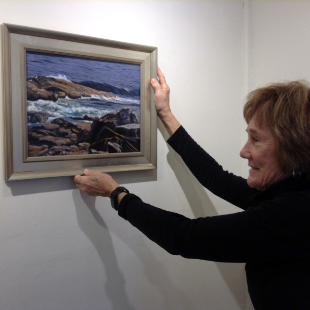 Artist Caroline Howe hangs one of her oil paintings.