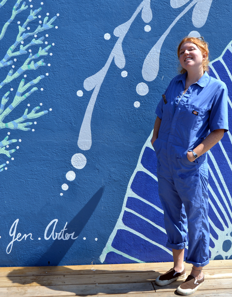 Artist Jenny Arter stands next to her signature on the recently completed mural at Oysterhead Pizza Co. in downtown Damariscotta. (Maia Zewert photo)