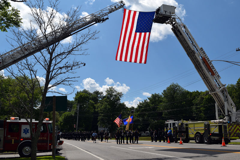 Fire trucks from Bath and Brunswick hold an American flag over Route 1 in Wiscasset, Saturday, Aug. 1, during a procession in honor of firefighter Richard Kubler. (Hailey Bryant photo)