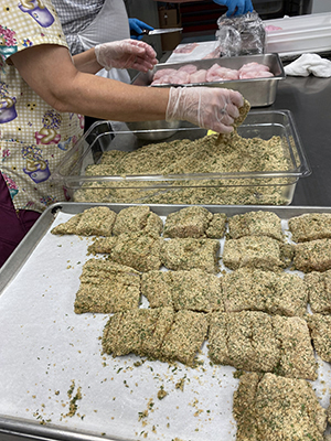 A worker breads hake fillets in an RSU 12 kitchen. (Photo courtesy Food Management)