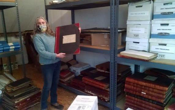 Bristol Town Clerk Rachel Bizarro holds a tax assessment ledger book in front of racks of old town records that are slated to be moved to the shared vault under construction at the Bristol History Center. (Photo courtesy Chris Hall)