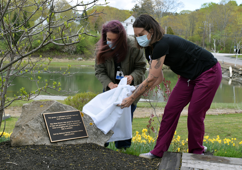 LincolnHealth employees Trudy DeLong (left) and Rebekah Oliver unveil a plaque on a stone in front of the suicide prevention awareness garden on the hospital's Miles Campus in Damariscotta during a dedication ceremony on Monday, May 10. (Evan Houk photo)