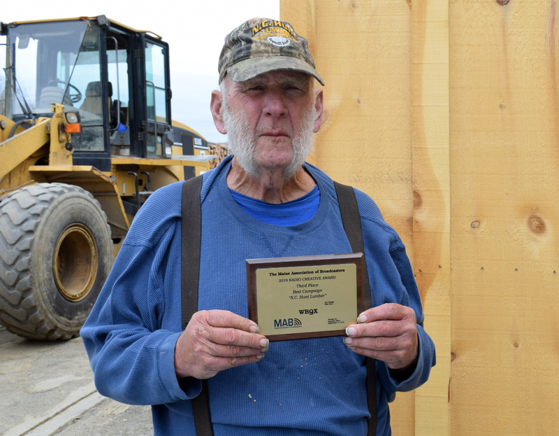 Eben Hunt holds a plaque recognizing N.C. Hunt for placing third in the Maine Association of Broadcasters' Best Campaign competition in 2019. Hunt voices the ads, but spends most of his days using the loader in the background to screen loam at the Jefferson lumberyard. (Evan Houk photo)