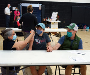 Great Salt Bay Community School eighth grader Tessa McNamara (center) holds hands with her father, Jay McNamara (right), while receiving a vaccination from LincolnHealth nurse and Lincoln Academy parent Angela Russ during a clinic at the high school on Tuesday, May 18.