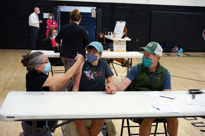 Great Salt Bay Community School eighth grader Tessa McNamara (center) holds hands with her father, Jay McNamara (right), while receiving a vaccination from  LincolnHealth nurse and Lincoln Academy parent Angela Russ during a clinic at the high school on Tuesday, May 18.