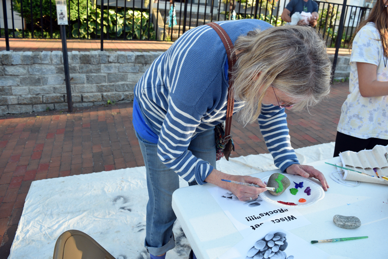 Margot Stiassni-Sieracki paints a mountain scene at the rock-painting station at the Wiscasset Art Walk on Thursday, June 24. (Nate Poole photo)