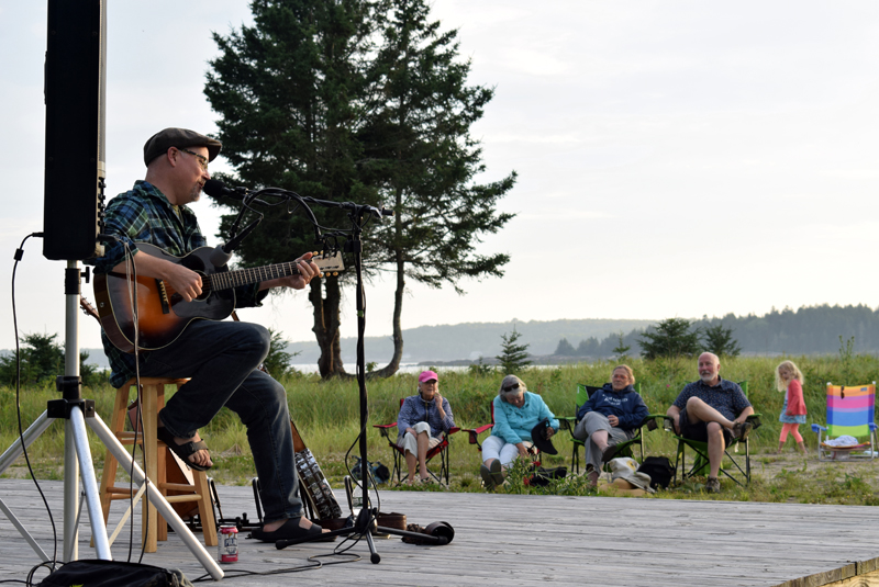 Jud Caswell plays a song on his guitar and sings at Pemaquid Beach during a fundraiser for the reconstruction of the Seagull Shop on Monday, July 12. More than $3,440 was raised during the event and the shop's owners say they plan to reopen by late July or August. (Evan Houk photo)