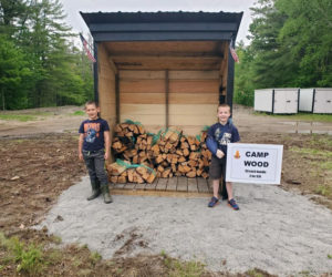 Zachary Hoppe and Ryan Parson stand in front of their camp firewood stand. The 7-year-olds plan to keep the stand open through Labor Day. (Photo courtesy Jessica Hoppe)