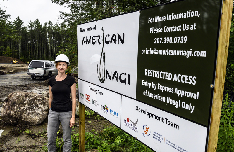 Sara Rademaker, founder and president of American Unagi, stands in front of a sign at the construction site for her 27,000 square foot facility in Waldoboro on July 19. Rademaker said this moment represents the dream she has had for seven years of building an aquaculture business in Maine. (Bisi Cameron Yee photo)