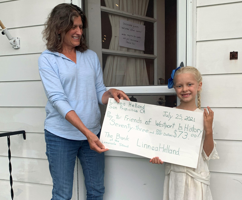Friends of Westport Island History Committee member Joan Mason-Bradford accepts a donation of $73 from 6-year-old Linnea Helland. Linnea raised the money at her lemonade stand during the town-wide yard sale on Sunday July 18. (Photo courtesy Gaye Wagner)