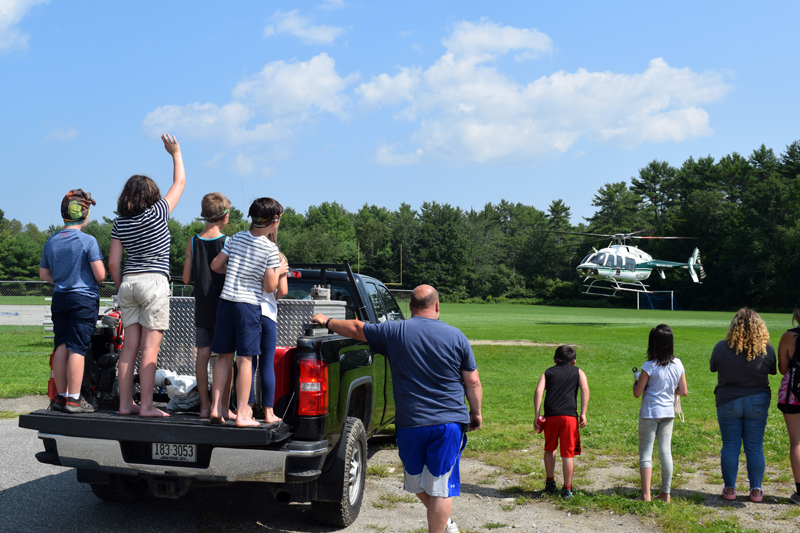Central Lincoln County YMCA campers wave from Maine Forest Ranger Daniel Welch's tailgate as Ranger Pilot Chris Blackie guides his helicopter away from the Great Salt Bay Community School's football field on Friday, Aug. 6. (Nate Poole photo)