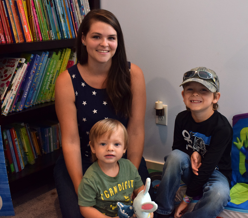 Newcastle resident Emily Krah sits with her two sons-- Raylan, 5, and Jace, one-and-a-half-- in front of a bookshelf at her home on Monday, Aug. 2. Krah has amassed a collection of nearly 600 children's books during her time working as an Usbourne Books & More seller. (Evan Houk photo)