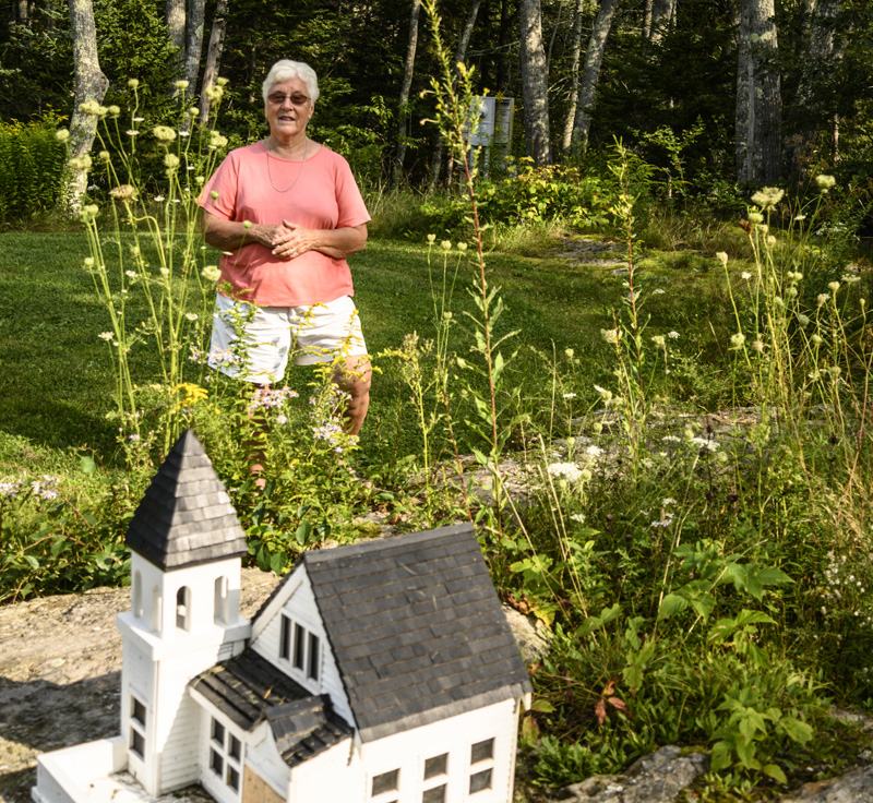 Donna Plummer stands behind a model of the Union Congregational Church on a rock ledge in her front yard in South Bristol. Plummer has been going to the full-sized version of the church since she was three years old.  (Bisi Cameron Yee photo)