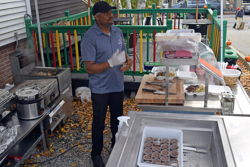 Peter Ebanks, co-owner of J &amp; J Jamaican Grocery and Gift Shop in Damariscotta, talks to a customer while frying plantains and filling orders on Oct. 17. On Saturdays and Sundays, the store offers smoked jerk chicken and pork that comes with sauteed vegetables, fried plantains, and rice and peas. (Evan Houk photo)