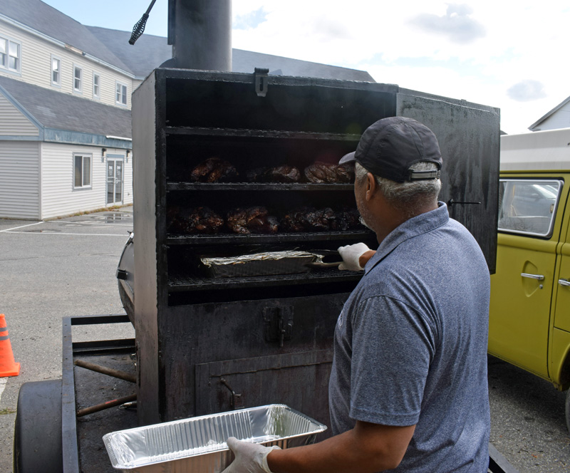 Peter Ebanks removes jerk chicken from his smoker in the back of the parking lot behind 88 Main St. He keeps the jerk chicken in a tin foil pan to retain the juices of the chicken so it doesn't dry out. (Evan Houk photo)