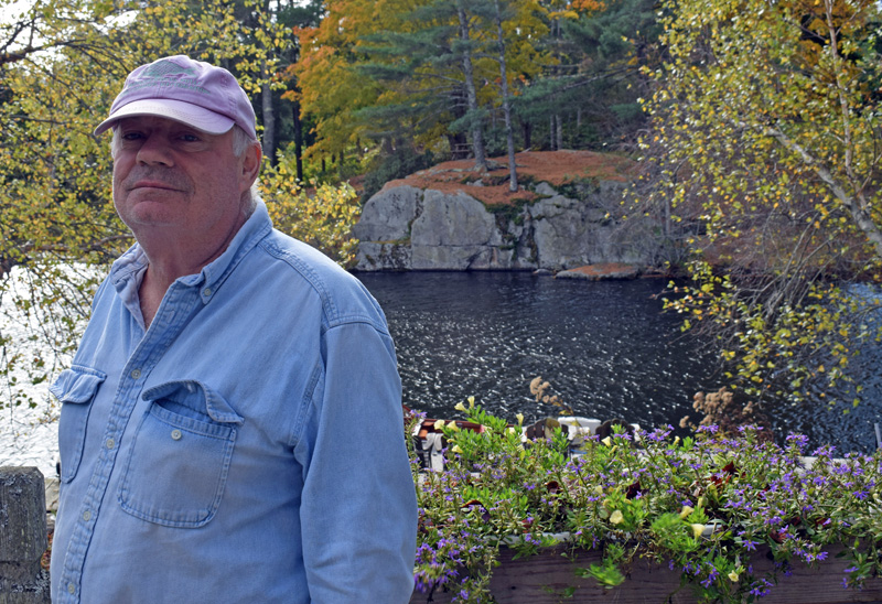 Bobby Whear, co-owner of the Mill Pond Inn, stands on the back deck of the bed-and-breakfast in front of the rock he said he always dreamed of shooting hockey pucks against. Unfortunately, the flowing water never froze. (Evan Houk photo)