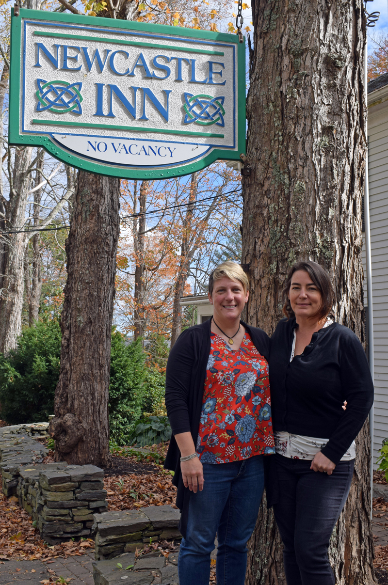 The new owners and operators of the Newcastle Inn, married couple Liz and Carolyn Cooke, stand by the sign for the River Road establishment. The duo plan to keep things the same for the time being at the beloved bed and breakfast. (Evan Houk photo)