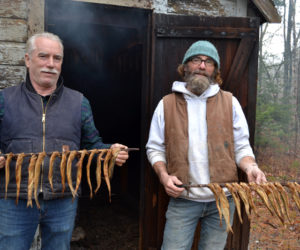 Brothers Ken (left) and Todd Lincoln hold strings of smoked herring in front of the old smokehouse next to the S Road School in South Bristol. (Maia Zewert photo)
