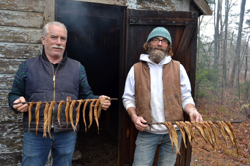 Brothers Ken (left) and Todd Lincoln hold strings of smoked herring in front of the old smokehouse next to the S Road School in South Bristol. (Maia Zewert photo)