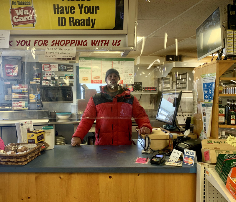 Yasser Alsudany, who purchased the Whitefield Superette on Jan. 27, stands at the cash register behind a sheet of plastic still hanging as a COVID-19 precaution. (Anna M. Drzewiecki photo)