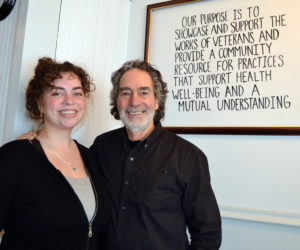 Olivia and Bernie DeLisle stand in front of The Peace Gallery's mission statement written on a whiteboard in its 122 Main St. headquarters in Damariscotta. The father and daughter opened the space earlier this week. (Maia Zewert photo)