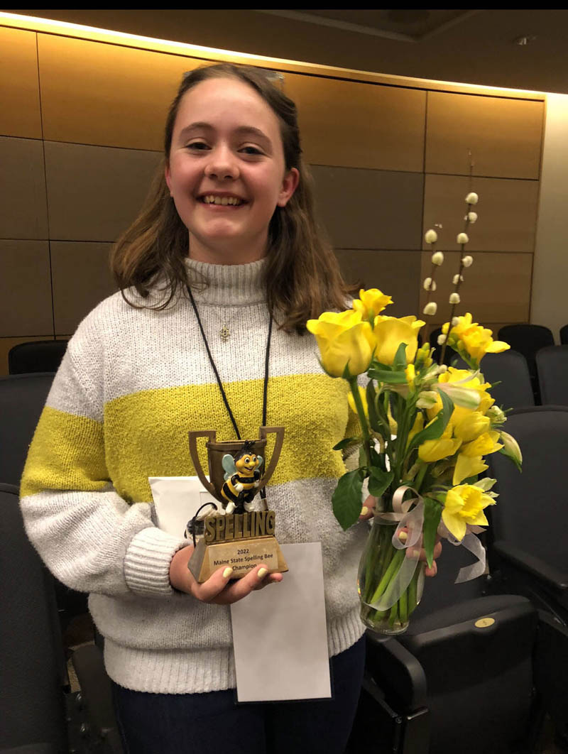 South Bristol School eighth grader Amelia Rice holds her trophy and a bouquet of yellow flowers after winning the Maine State Spelling Bee on March 26. Rice coordinated her outfit for the occasion, wearing a striped sweater and a honeycomb necklace. (Photo courtesy Susan Bartlett Rice)