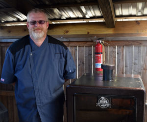 Christian "Chris" Grant, owner of Gator's Deep South BBQ in Damariscotta, stands in his chef's jacket next to one of the smokers at the 603 Main St. location. The eatery is open every day from 11 a.m. to 8 p.m. (Evan Houk photo)