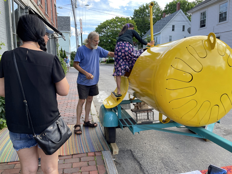 Instrument maker Jim Doble (center) brought his Yellow Submarine, played from the inside, to Wiscasset Art Walk in June. Doble will make a raw log amadinda for visitors to play during the Thursday, July 28 art walk, from 5-8 p.m. (Photo courtesy Wiscasset Art Walk)