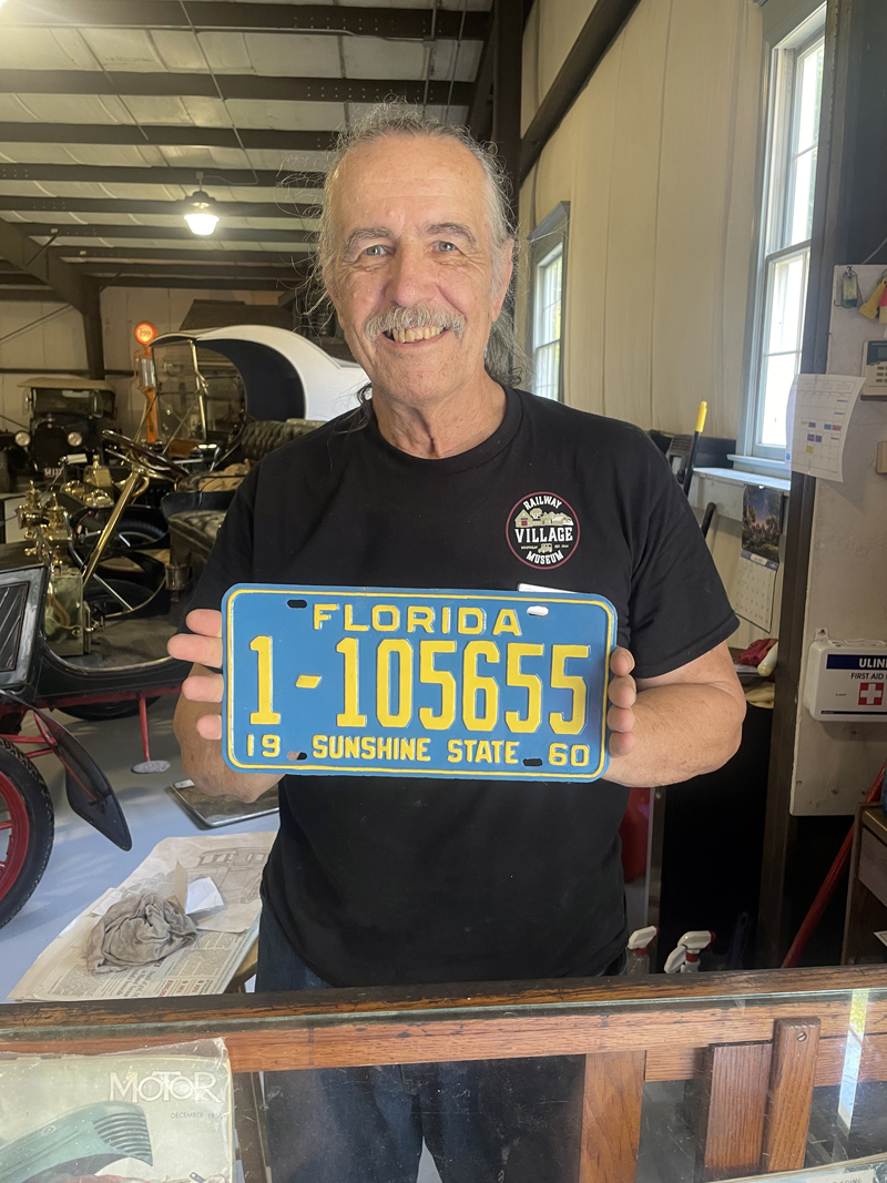 Larry Burridge shows off a vintage license plate he cleaned and refurbished, another hobby he has developed related to his passion for antique automobiles. (Sherwood Olin photo)