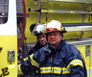 Donnie Leeman (right) stands by the door of a Newcastle fire truck. Leeman was an 18-year volunteer with Newcastle, including serving as assistant chief. (Photo courtesy Newcastle Fire Department)