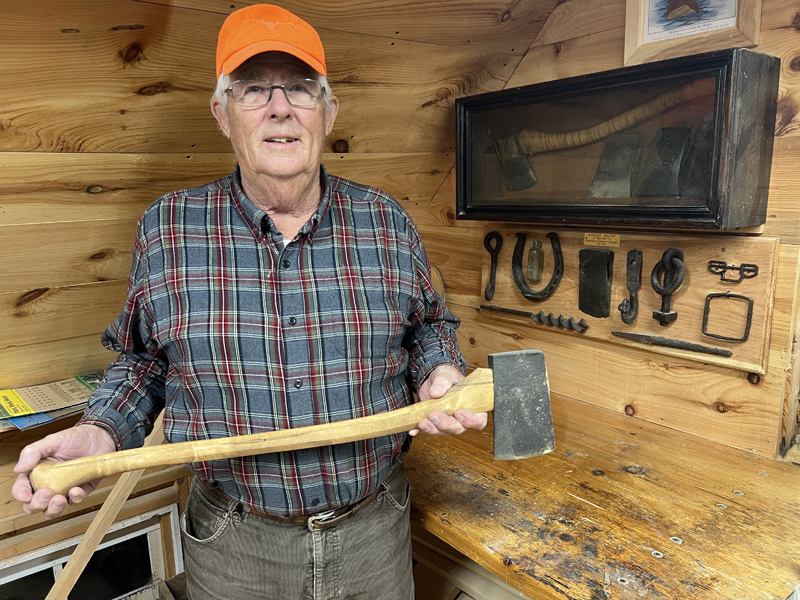 Donnie Johnston, of Jefferson, holds an ax in front of a display case of items found by Joe Holland and himself at the site of an old logging camp on the West Branch. (Photo courtesy Joe Holland)