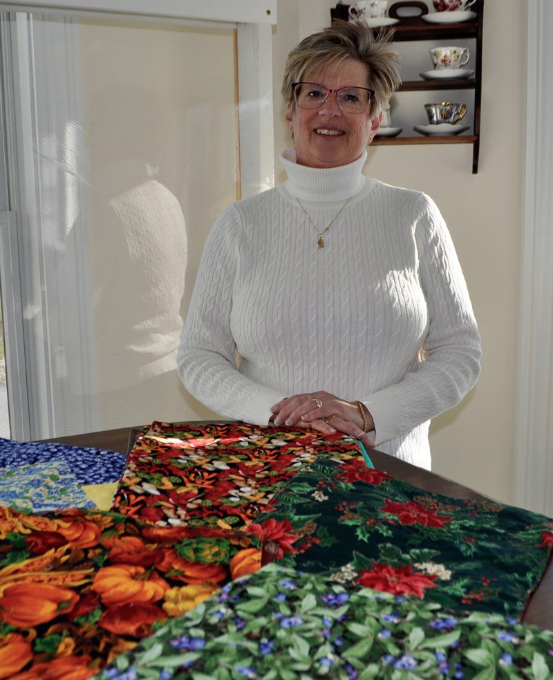 Deb Boucher, the charity coordinator for the Clamshell Quilters, with  sampling of the beautiful placemats the group donated to One2One Care's Meals at Home program. (Photo courtesy Kim Traina)