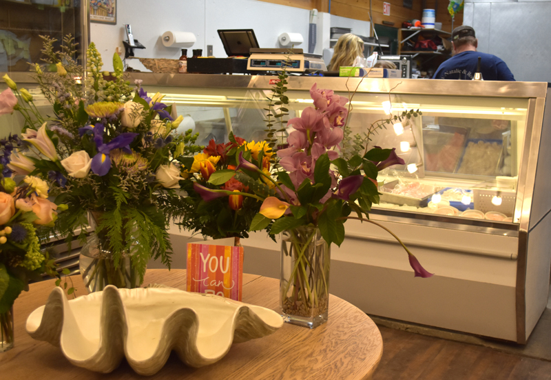 Congratulatory flowers from local businesses decorate a table at Simmons Seafood Market at 49 Main St. in Damariscotta while the Simmons family, who said they are excited to be part of the community, works behind the counter. The direct-to-consumer market is in a soft opening and will celebrate a grand opening on Friday, Feb. 3. (Elizabeth Walztoni photo)